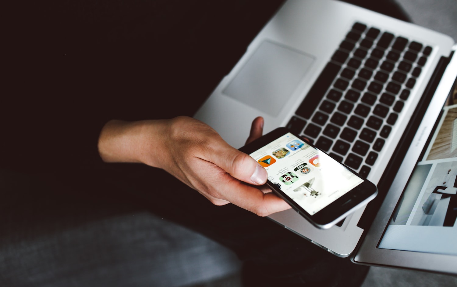 A person browsing a product menu on a smartphone held above an open laptop
