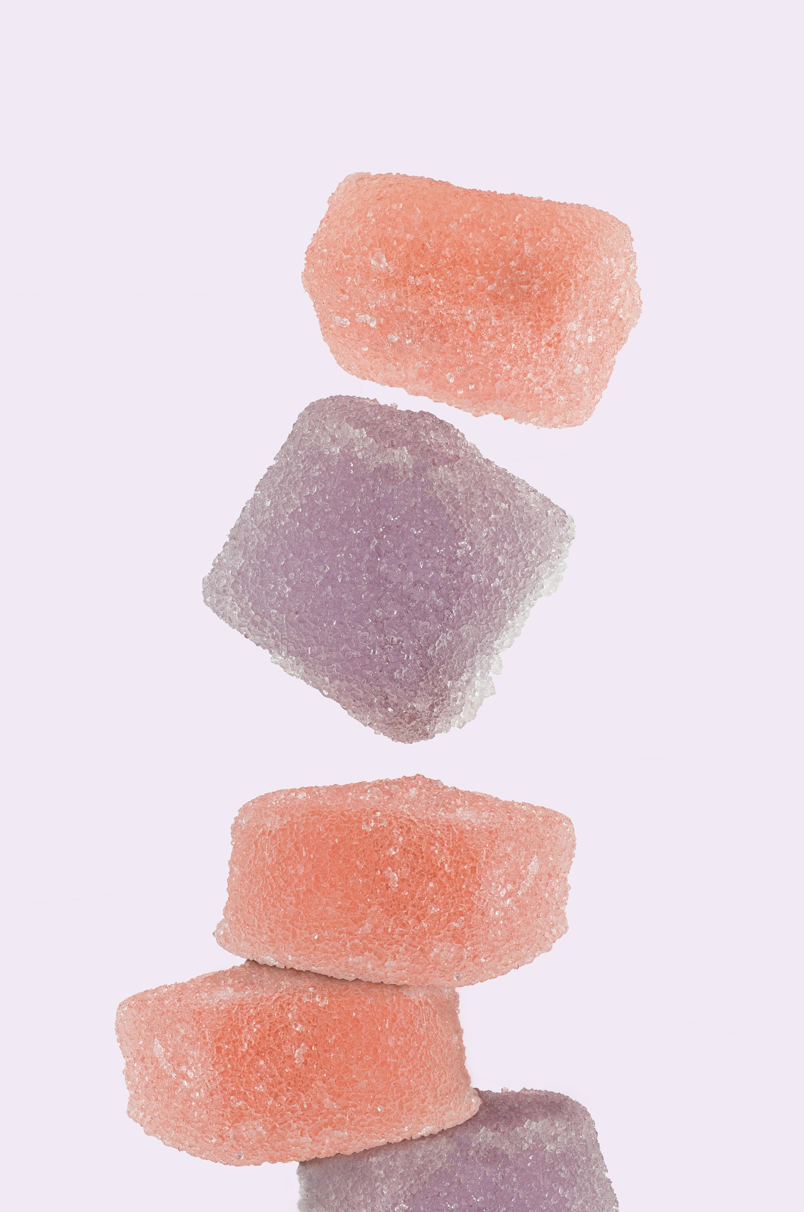 Sugar-coated cannabis gummies in several flavors stacked against a pale background