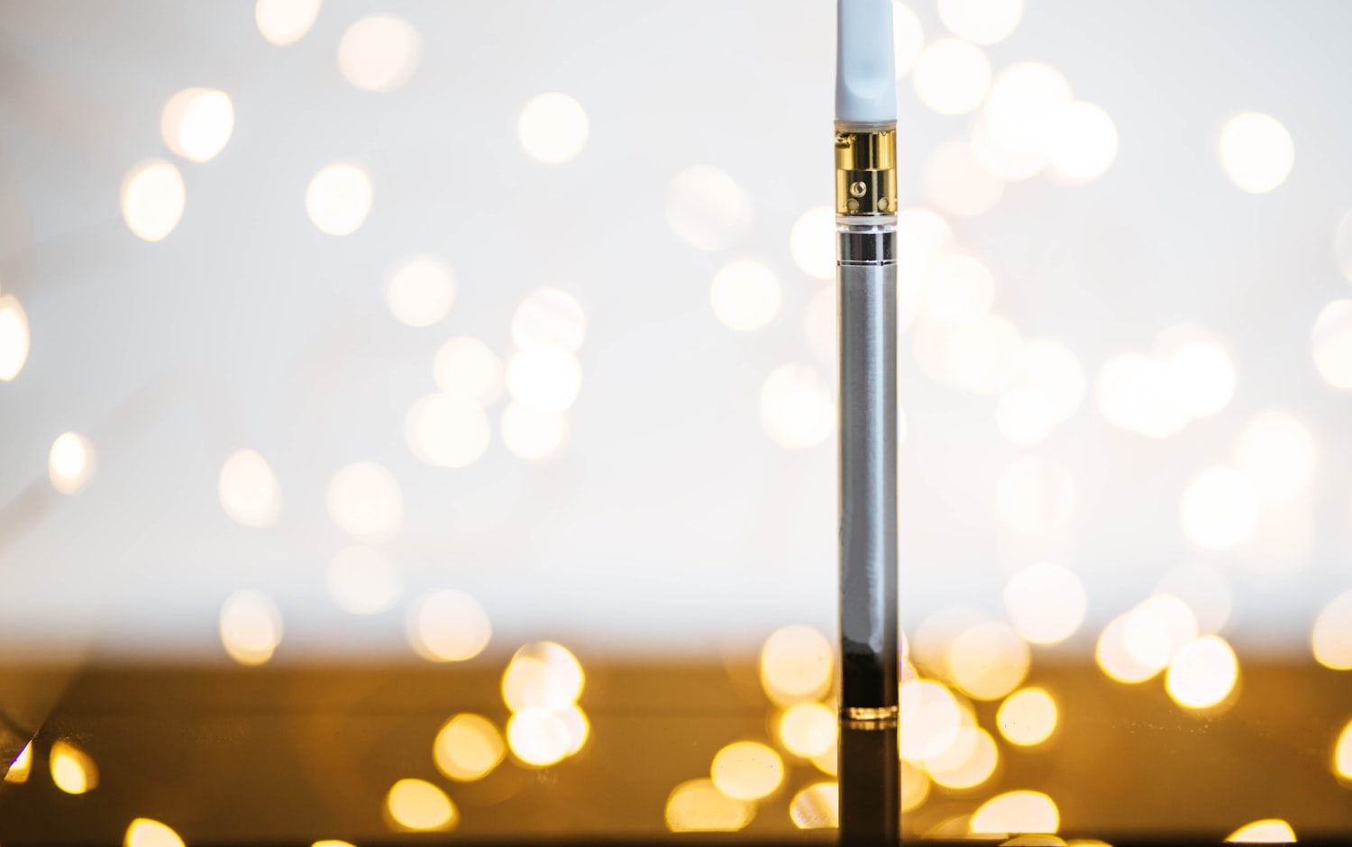 A 510-thread cannabis vape cartridge attached to a slim battery, lit against a bokeh background